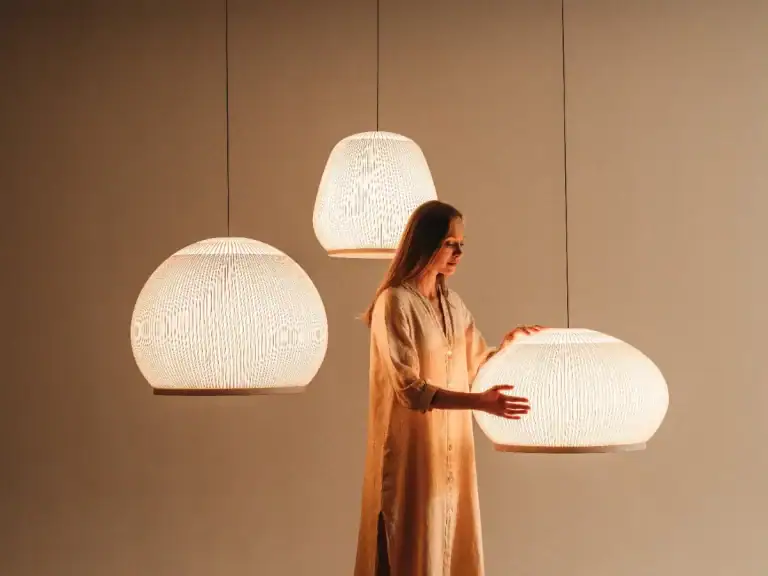 A person beside three Vibia Knit pendants in different shapes, glowing through ribbed knit