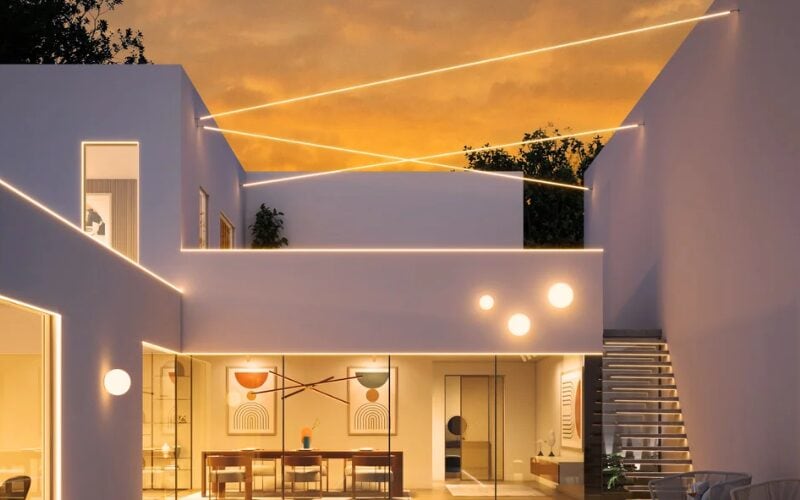Modern white home at dusk with linear cove lighting tracing the double-height ceiling.