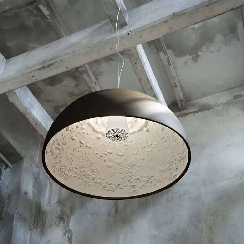Flos Skygarden pendant seen from below, its plaster-patterned interior lit, under concrete beams