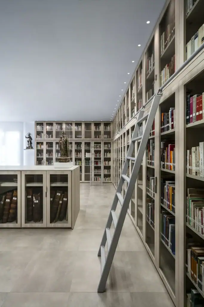 Library with floor-to-ceiling bookshelves and a ladder, with a line of small Flos Light Shadow Dots downlights in the ceiling