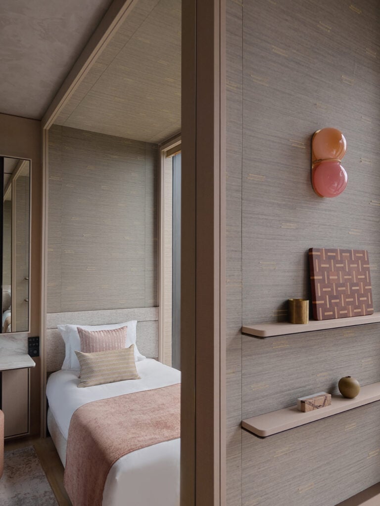 SkLO Twin sconce in peach and pink glass on a bedroom wall above floating shelves