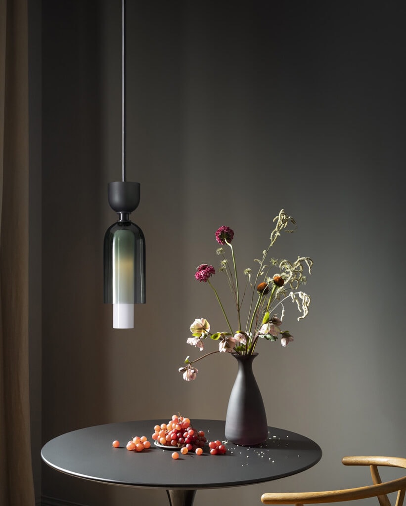 Modern black pendant light over a round table with a vase of flowers and scattered berries.