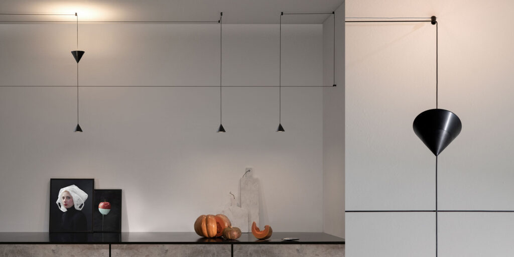 Karman Filomena black cones on thin cables along a wall and ceiling above a sideboard