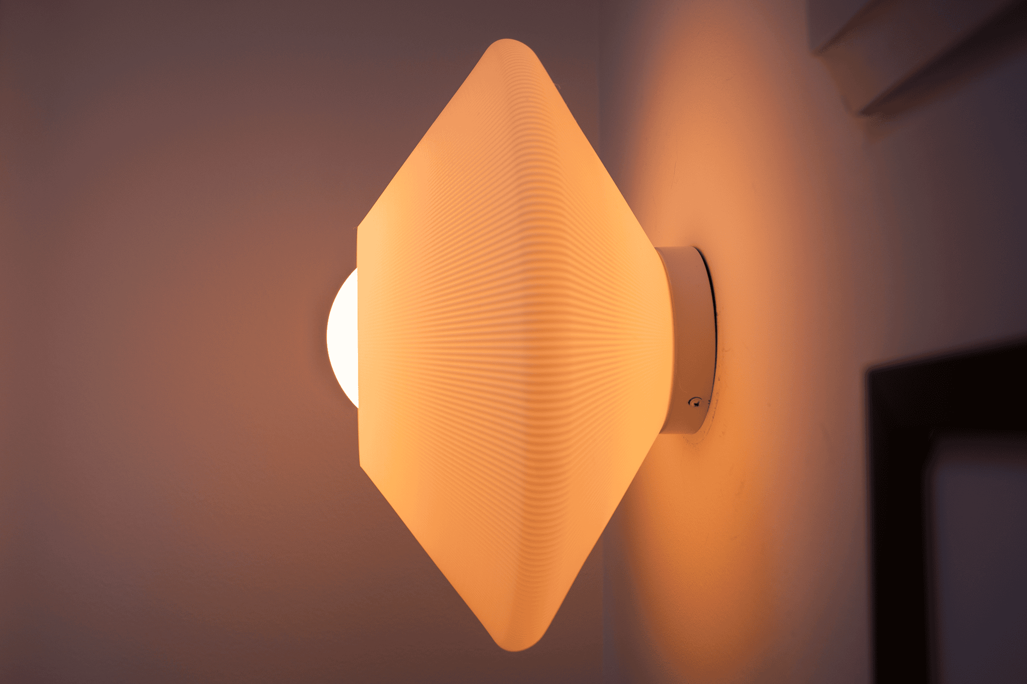 Giraffe Ripple sconce in off-white from the side, lit, its bulb at the face