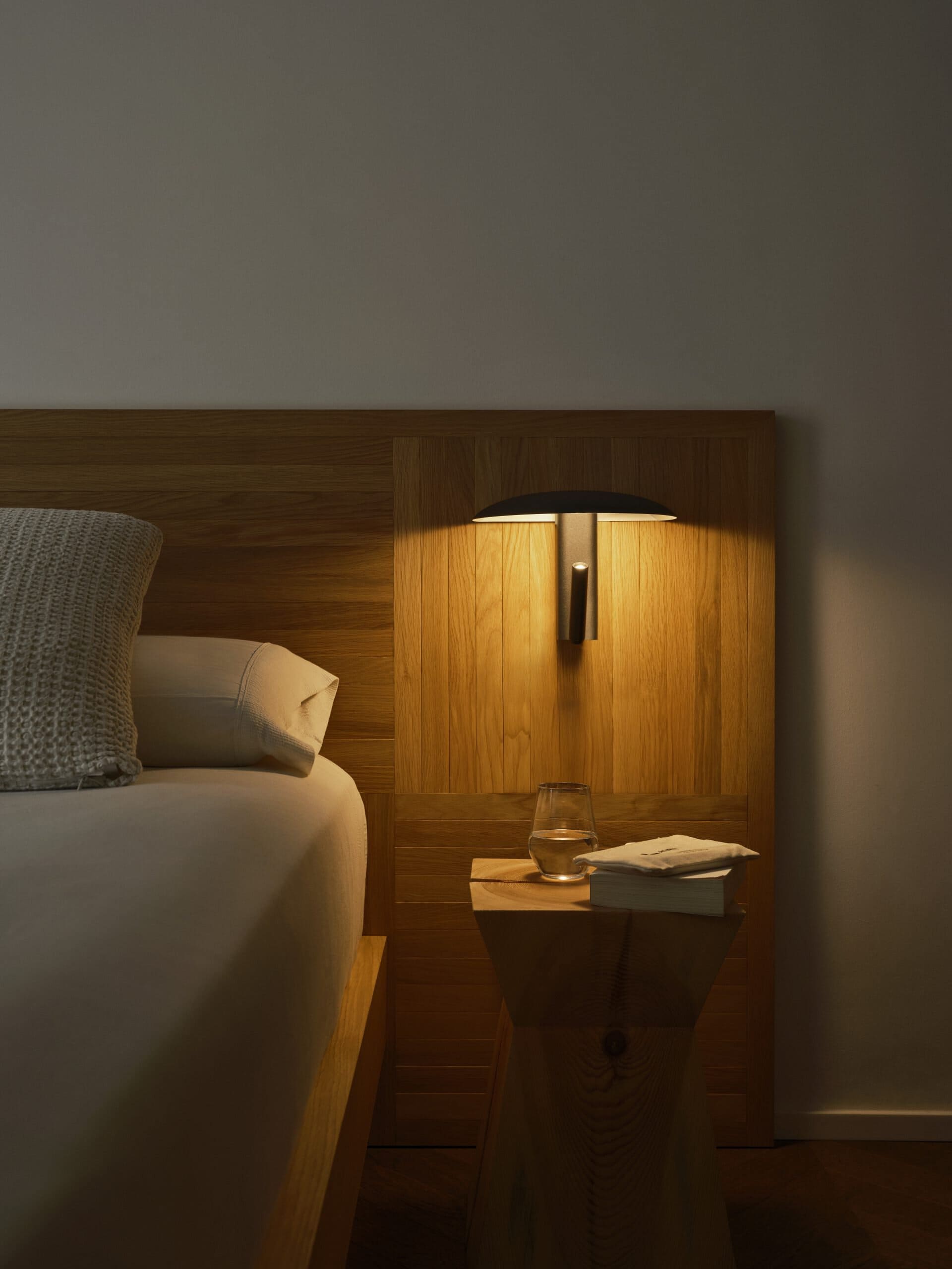 Marset Konoha wall light in black above a bedside table, lit as a reading light